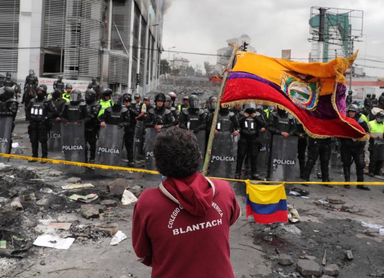 Un hombre ondea una bandera ecuatoriana frente a los miembros de la policía que acordonan y custodian los alrededores de la Contraloría ecuatoriana este domingo, luego de que fuera tomada y atacada ayer por manifestantes, en Quito. FOTO EFE