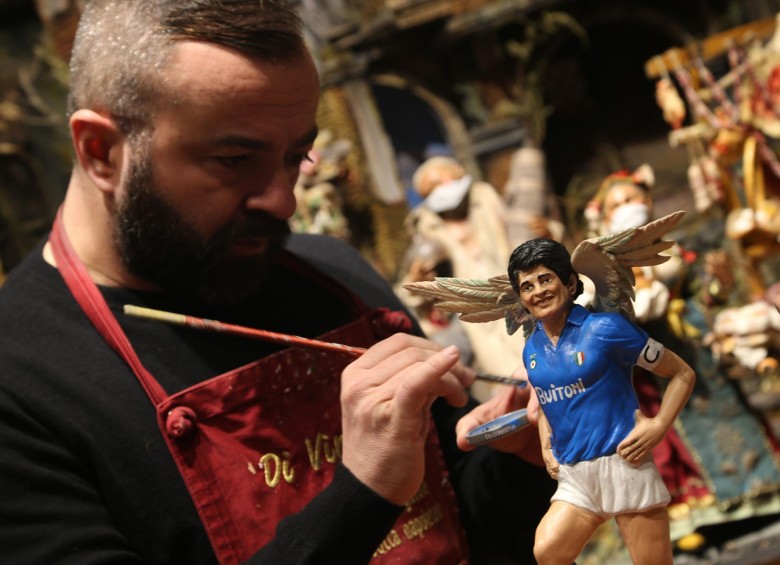 En esa misma ciudad, un artista pinta una pequeña escultura de Maradona con alas y vistiendo el uniforme de Nápoles. FOTO AFP