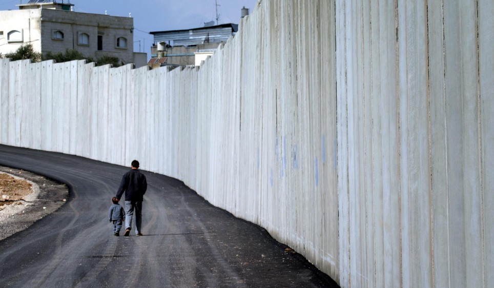 Un hombre y un niño caminan junto a un muro de concreto que forma parte de la barrera de seguridad que separa a Israel de Cisjordania, en Baqa El Gharbiya. FOTO REUTERS