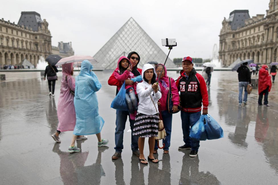 Turistas posan cerca de la Pirámide del Museo del Louvre en un día de verano lluvioso en París. FOTO: Charles Platiau / REUTERS