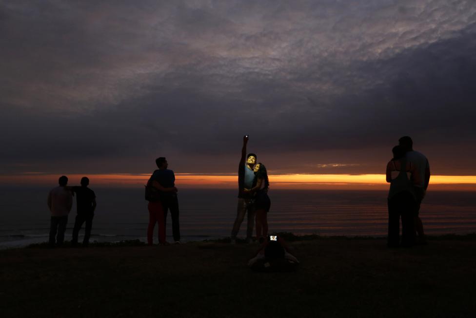 Esta pareja posa para una foto mientras otros observan la puesta de sol frente al mar en el barrio de Miraflores, en Lima, Perú. FOTO: Mariana Bazo / REUTERS