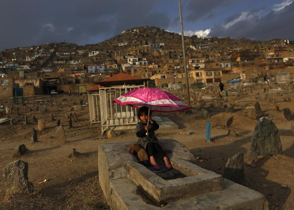 Una niña sostiene un paraguas sentada en una tumba en un cementerio de Kabul, Afganistán, el 12 de febrero de 2015. FOTO REUTERS